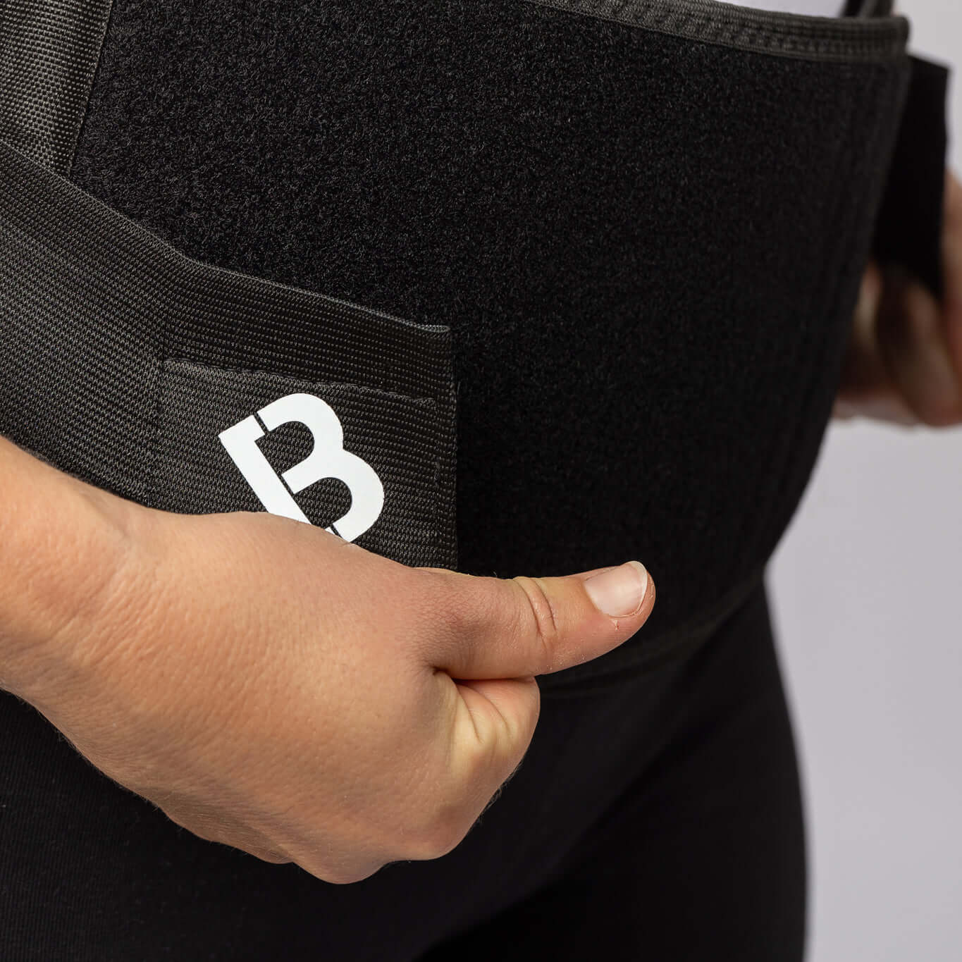 A woman's hand pulling the black BioMagnetic Back Support belt closed at the front. 