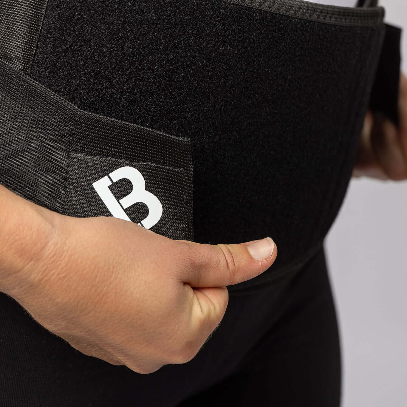 A woman's hand pulling the black BioMagnetic Back Support belt closed at the front.