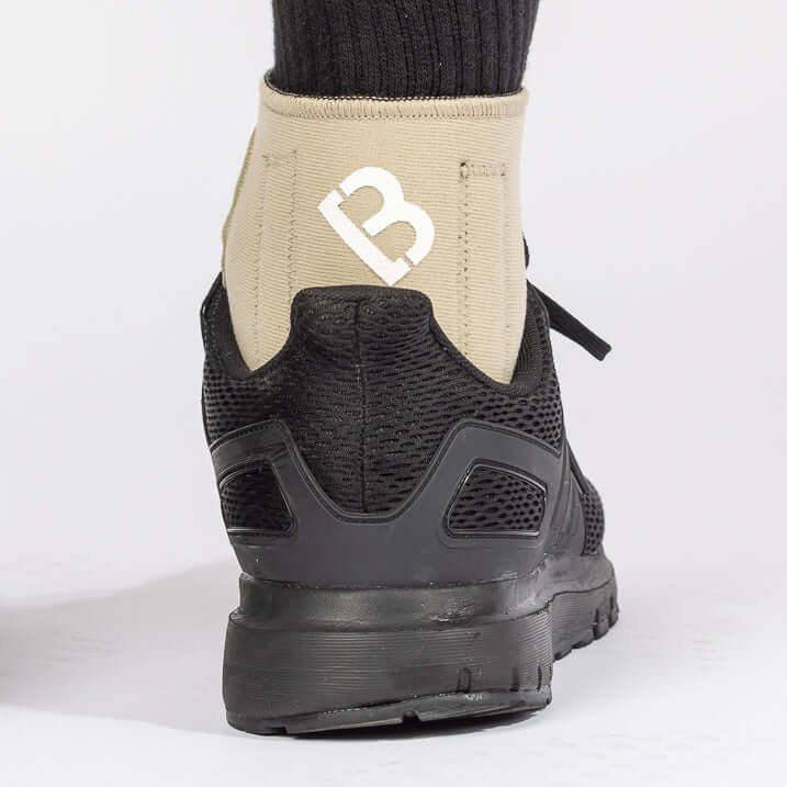 The BioMagnetic Ankle Support in beige being worn by a man wearing a black shoe, showcasing how the magnetic ankle support can be worn with most footwear. The view is from the back of the ankle.