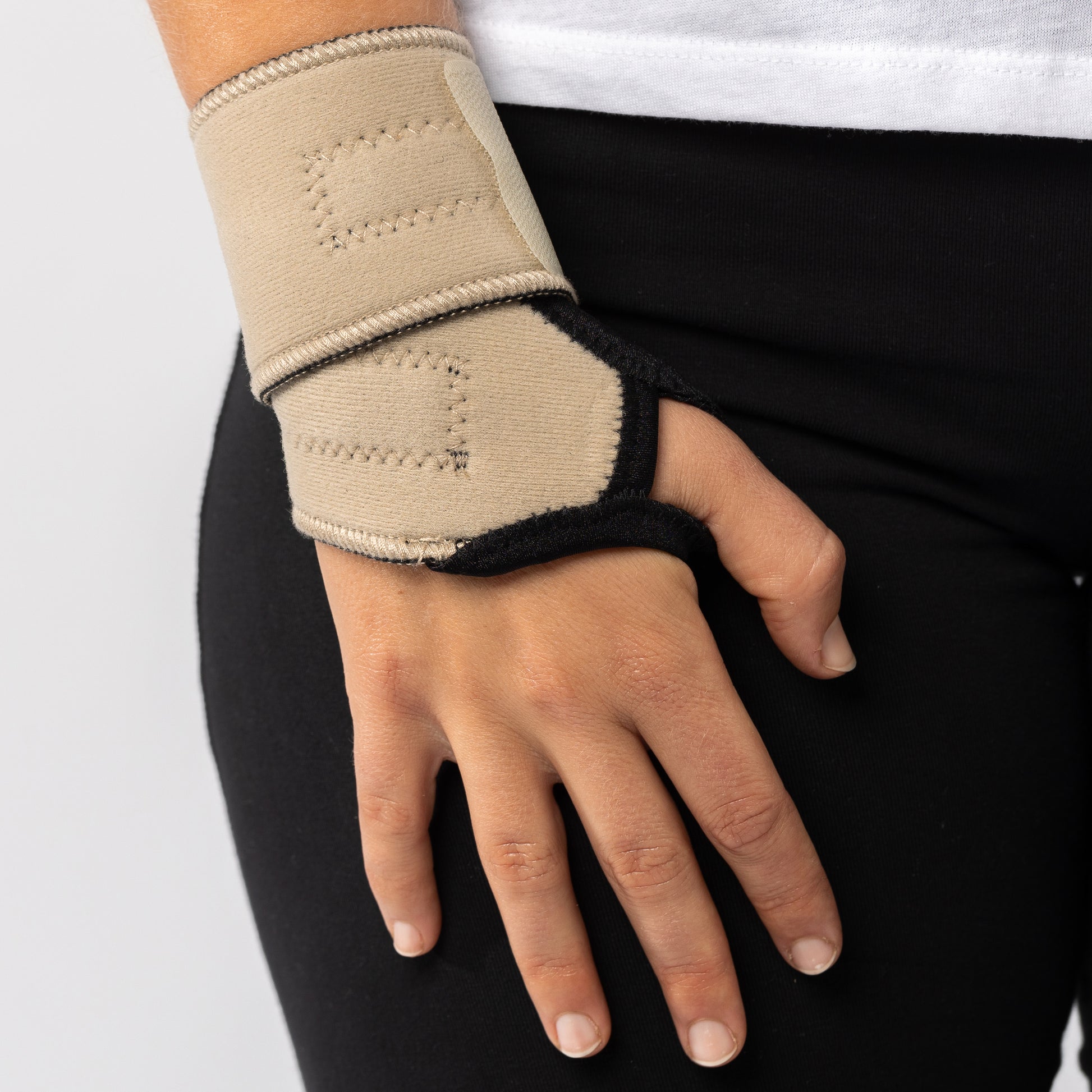 Woman placing hand on her right thigh while wearing a beige Bio magnetic Wrist Support around her wrist.