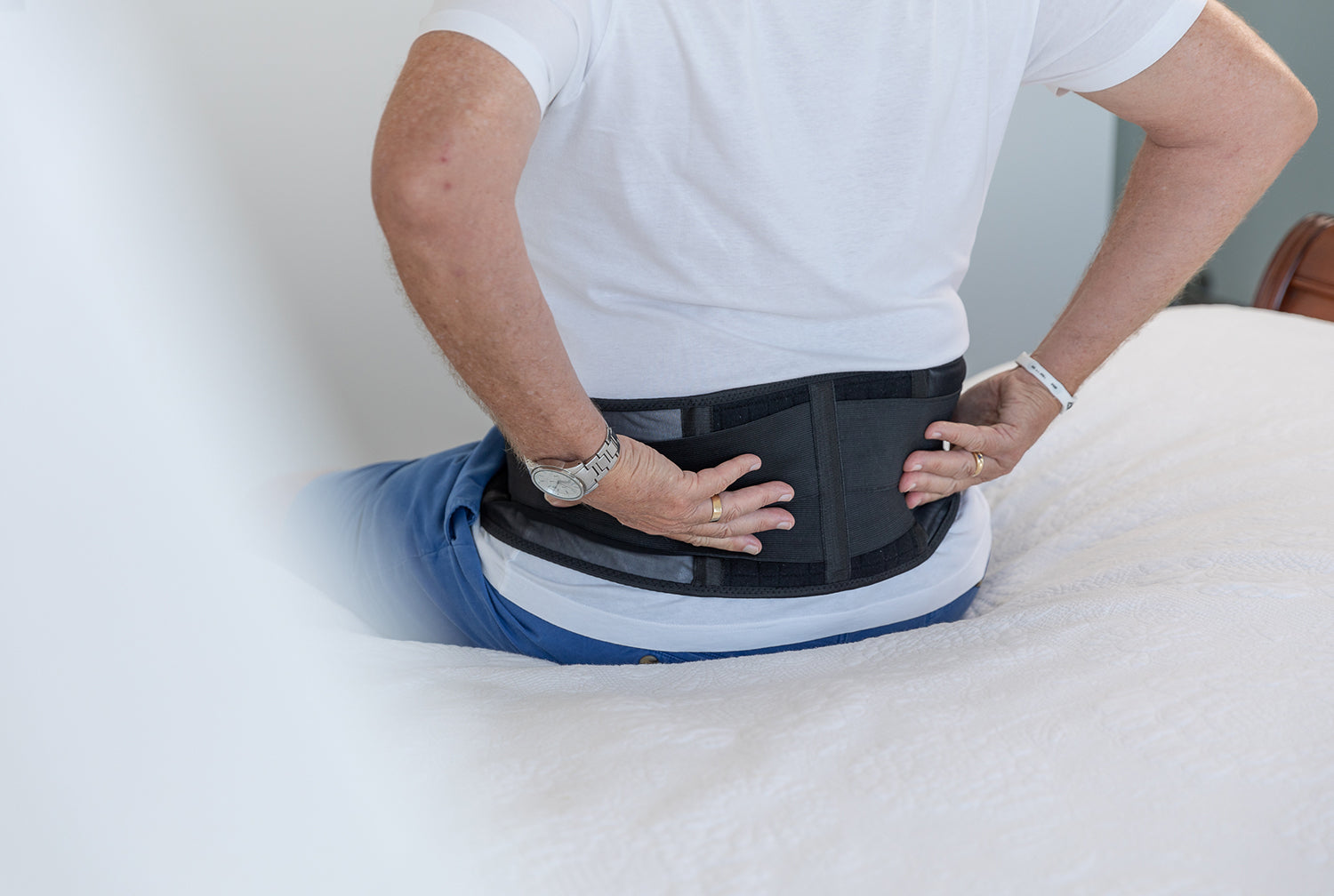 Man holding back in pain wearing magnetic back support on bed. 