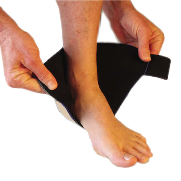 The Bio Magnetic Ankle Support in beige being put on by a person. The magnetic ankle support has been cupped around the ball of the foot and the person is holding the adhesive closure. This is step one of the how to wear process for the magnetic ankle support. 