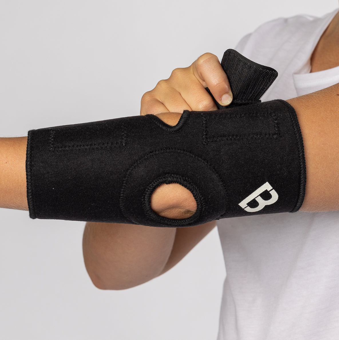 Woman putting on the BioMagnetic Black Elbow Support, the last velcro is being put on to secure the elbow support onto her arm. 