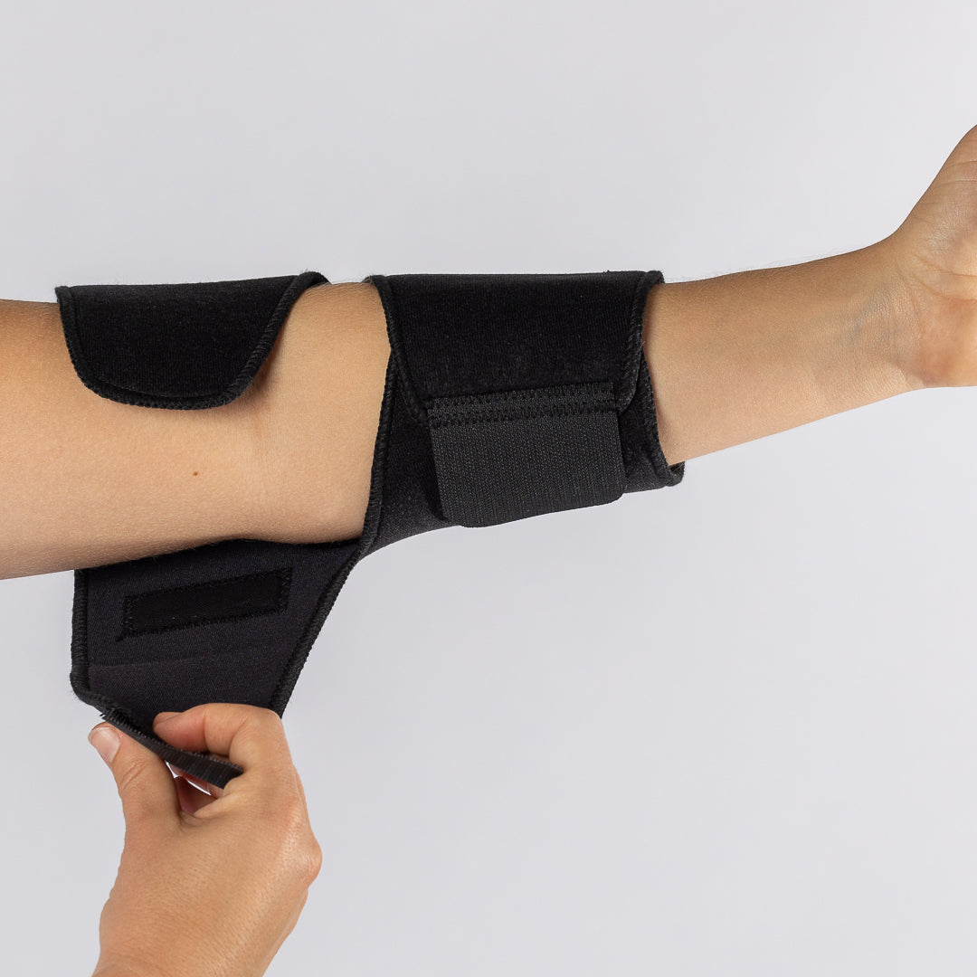 The Bio Magnetic Elbow Support in Black being put on by a woman showing how to put on the support. 