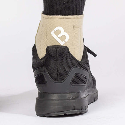 The BioMagnetic Ankle Support in beige being worn by a man wearing a black shoe, showcasing how the magnetic ankle support can be worn with most footwear. The view is from the back of the ankle. 