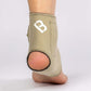 The Bio Magnetic Ankle Support in Beige being worn on the right foot with the view from the back, showing the heel hole for added comfort. The 8 therapeutic magnets can be seen sewn into the sides of the support around the ankle. 