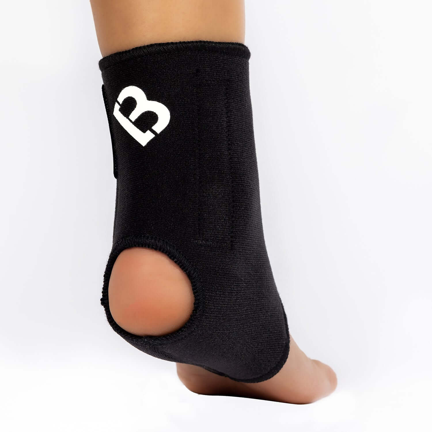 The Bio Magnetic Ankle Support in Black being worn on the right foot with the view from the back, showing the heel hole for added comfort. The 8 therapeutic magnets can be seen sewn into the sides of the support around the ankle. 