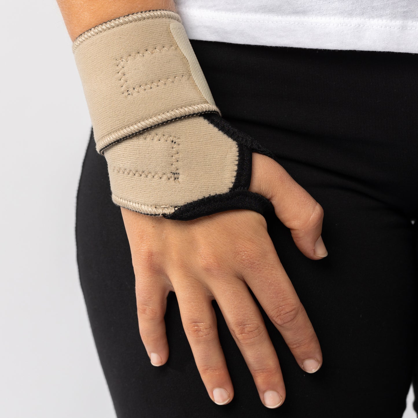 Woman placing hand on her right thigh while wearing a beige Bio magnetic Wrist Support around her wrist. 