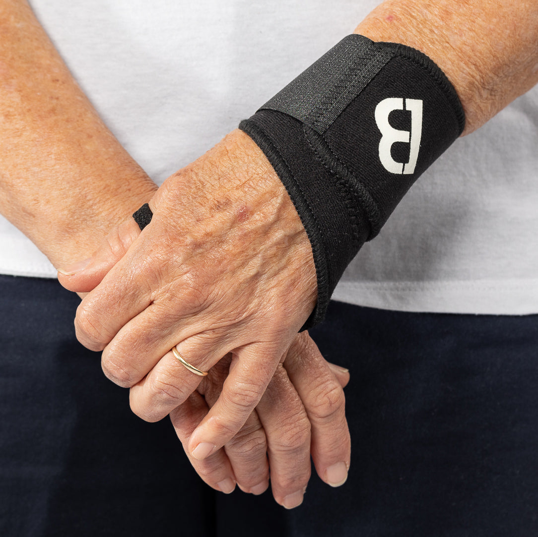 Woman's elderly hands wearing a black Bio Magnetic Wrist Support on her left hand.