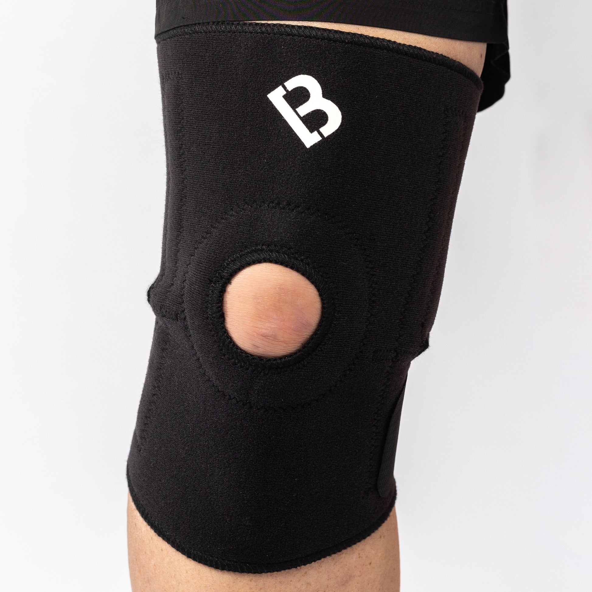 Bio Magnetic Knee Support worn by a man and viewed from the front displaying the hole on the knee cap for increased flexibility. The magnetic knee support in black is being worn on the right leg.